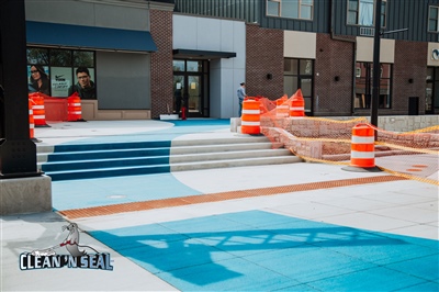 A newly painted blue and white concrete area with stairs in front of a building, marked with orange safety barrels and cones.