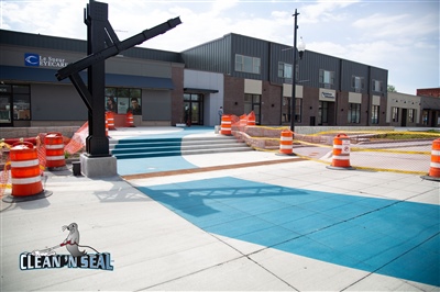 A newly painted blue and white concrete area with stairs in front of a building, marked with orange safety barrels and cones.