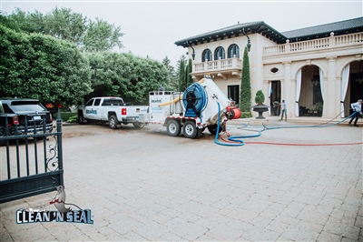 A worksite in front of a large, elegant building with arched windows and doors, featuring a truck and a trailer-mounted pressure washing unit.
