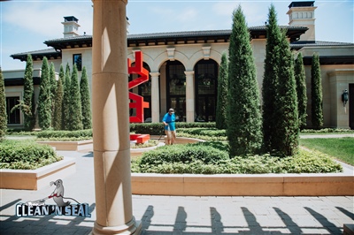 A well-maintained garden in front of an elegant building with arched windows and tall shrubs, featuring a red sculpture and a worker in a blue shirt.